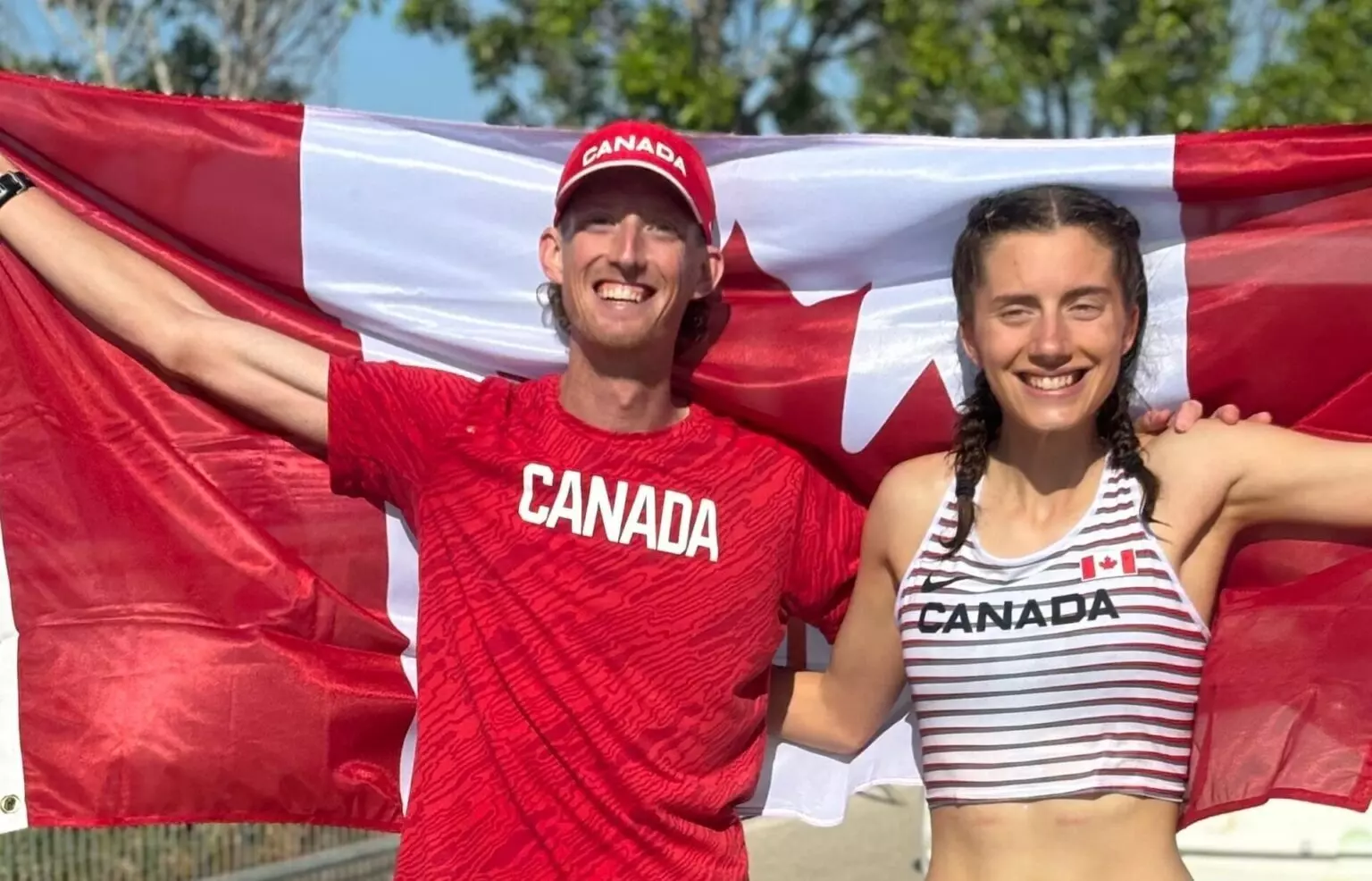 Race walkers Evan Dunfee and Olivia Lundman grinning at the camera and holding up a Canadian flag